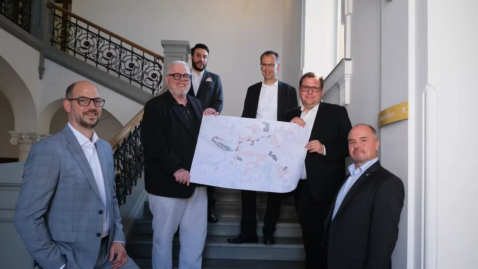 Treppenhaus Rathaus Krefeld, Mitarbeiter der Stadt Krefeld und Deutsche Glasfaser halten einen Stadtplan in die Kamera, nachdem die Kooperationsvereinbarung unterschrieben wurde